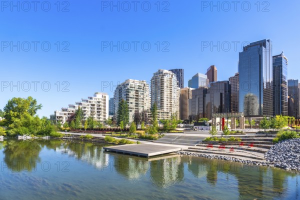 Modern buildings of downtown calgary reflecting in the calm water of a pond in st. Patrick's island park during a sunny summer day, creating a peaceful urban oasis