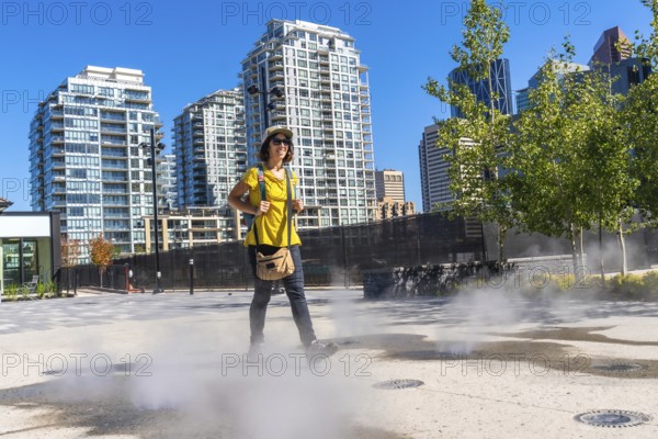 Female tourist walking in a foggy square in calgary city center during a sunny summer day, enjoying her urban exploration of the canadian metropolis
