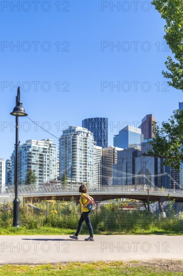 Young woman tourist walking in a city park in calgary, canada, enjoying the summer weather and urban scenery with modern skyscrapers and a pedestrian bridge