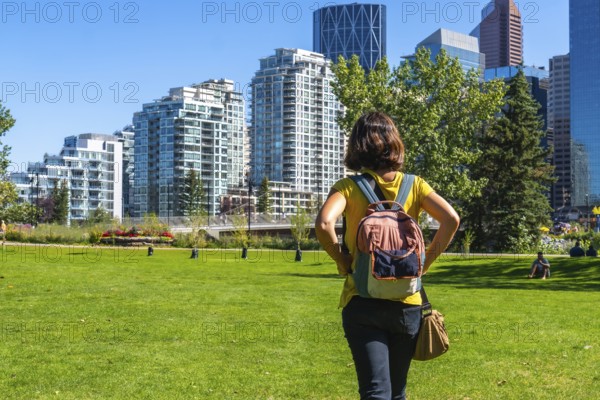 Female tourist with a backpack enjoying a sunny day in calgary's park, taking in the stunning views of the modern skyline and vibrant urban landscape surrounding her