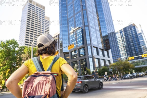 Young female tourist with backpack admiring modern skyscrapers in calgary's downtown district, a vibrant metropolis in alberta, canada, enjoying urban exploration and sightseeing
