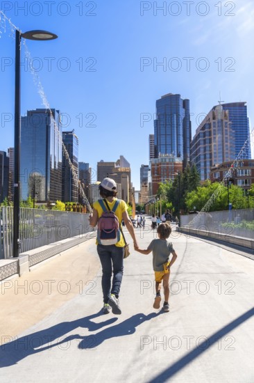 Mother and son enjoying a sunny day walking on a bridge in calgary city center, with skyscrapers and modern architecture in the background, representing family time and urban exploration