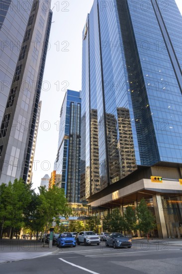 Glass skyscrapers reflecting surrounding buildings rise high above a street with cars passing by in calgary, alberta, canada, creating a dynamic urban scene during the day