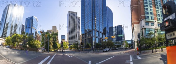 Panoramic view capturing calgary's downtown core, featuring modern office towers, vibrant traffic lights, busy crosswalks, and lush green trees under a bright sunny sky