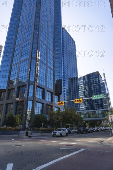 Cars navigating a busy street lined with modern skyscrapers, reflecting the vibrant blue sky in calgary's bustling downtown business district, showcase the city's dynamic urban landscape