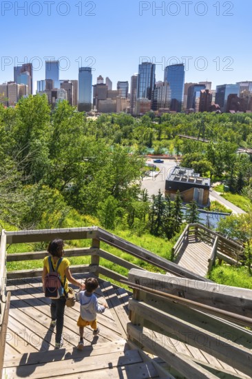 Mother and son descending a wooden staircase in a park, enjoying a picturesque view of the calgary city skyline on a sunny day, showcasing urban life amidst nature
