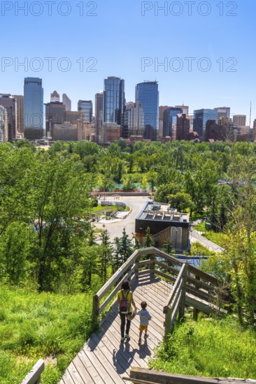 Mother and son walking down wooden stairs in a park, enjoying the view of the calgary skyline on a sunny summer day, showcasing urban nature and family tourism