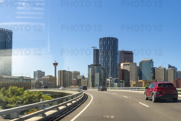 Cars driving along a highway showcase the vibrant calgary skyline, featuring the iconic calgary tower, under a bright blue sky on a sunny summer day