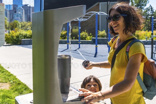 Mother and her son are filling a reusable water bottle at a public drinking fountain in a park in calgary, alberta, promoting hydration and sustainability