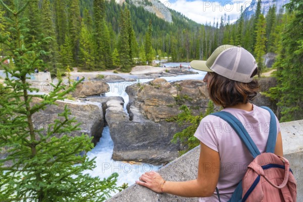 Female tourist wearing a baseball cap and backpack, admiring the bow river natural bridge in banff national park, alberta, a stunning landmark shaped by erosion