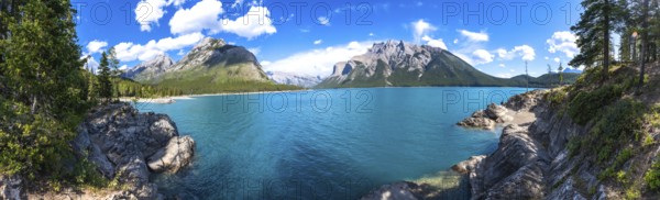 Breathtaking panoramic view of turquoise lake minnewanka surrounded by majestic rocky mountains under a vibrant blue sky with fluffy clouds in banff national park, alberta
