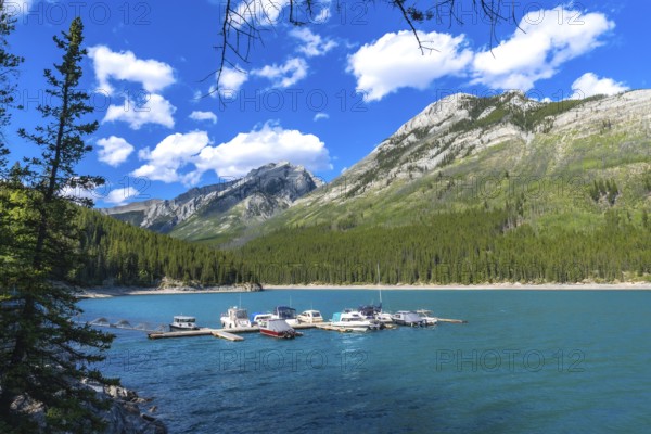 Many motorboats are resting on the turquoise waters of lake minnewanka, surrounded by the imposing canadian rockies, a beautiful summer day at banff national park, alberta, canada