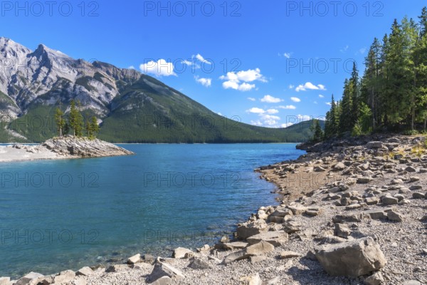 Breathtaking turquoise water of lake minnewanka reflecting the majestic canadian rockies under a vibrant blue sky creates a stunning summer landscape in banff national park, alberta, canada