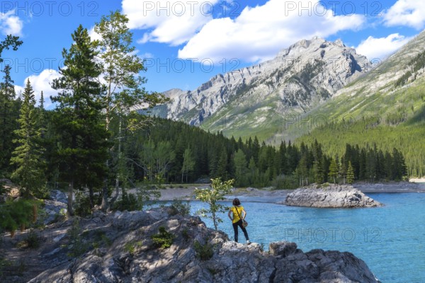 Tourist standing on rocks by the turquoise waters of lake minnewanka, admiring the breathtaking views of the canadian rockies and lush forests in banff national park