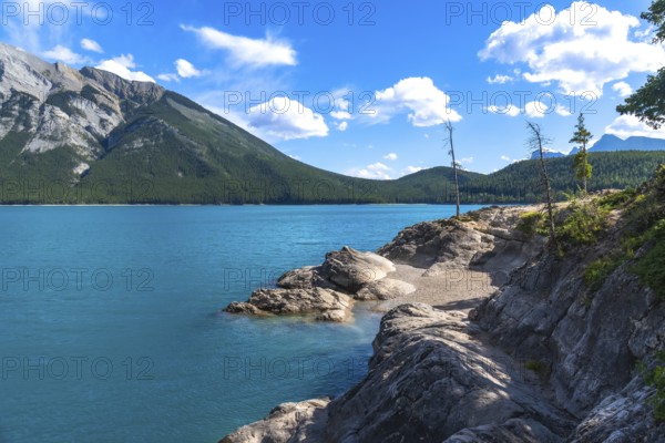 Breathtaking turquoise waters of lake minnewanka reflecting the majestic canadian rockies under a vibrant blue sky with scattered clouds in banff national park, alberta