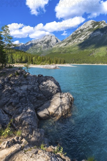 Breathtaking turquoise waters of lake minnewanka reflecting majestic rocky mountains under a vibrant blue sky with fluffy clouds in banff national park