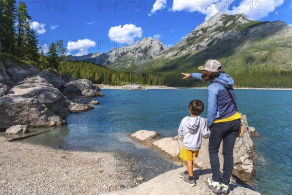 Mother points across the turquoise expanse of lake minnewanka, sharing a moment of awe with her son amidst the stunning scenery of banff national park's canadian rockies