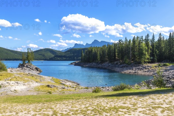 Turquoise waters of lake minnewanka reflecting a sunny sky with fluffy clouds, surrounded by lush forests and the majestic peaks of the canadian rockies in banff national park