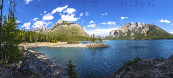 Sunlight illuminating the turquoise waters of lake minnewanka, reflecting surrounding mountains and a small island of evergreen trees in banff national park