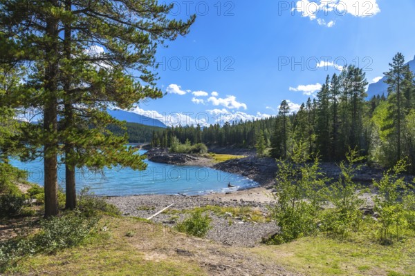 Vibrant turquoise waters of lake minnewanka sparkling under a sunny sky, framed by lush forests and the majestic canadian rockies in banff national park, alberta