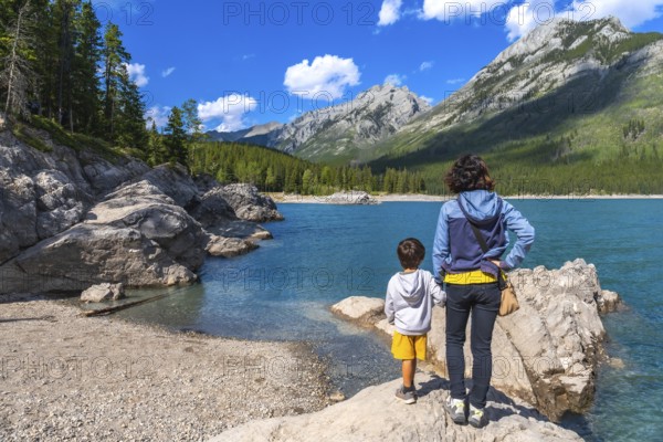 Mother and son standing on a rock, admiring the stunning turquoise waters of lake minnewanka, surrounded by the majestic canadian rockies on a sunny day