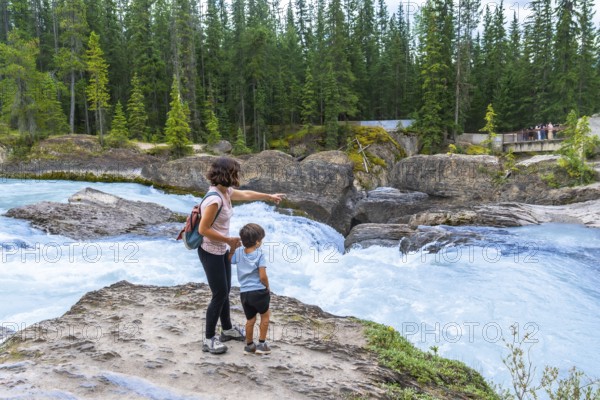 Mother and son enjoying the stunning view of bow river's natural bridge in banff national park, with turquoise waters rushing beneath a lush pine forest backdrop