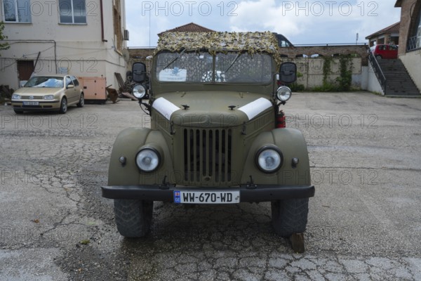 A green vintage car is parked in front of a building, Soviet all-wheel drive off-road vehicle, GAZ-69, Georgia