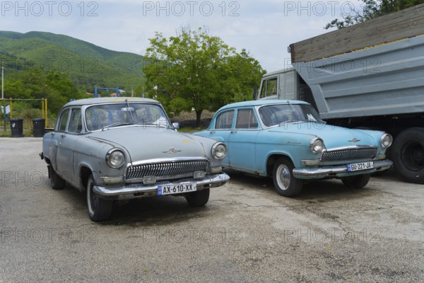 Two vintage cars are parked in a parking lot in front of a hilly landscape, GAZ M-21 Volga, Georgia