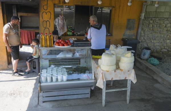 Market stall with cheese and tomatoes surrounded by a few people in an urban environment selling cheese, tomatoes and oil, Badiauri, Kakheti region, Georgia
