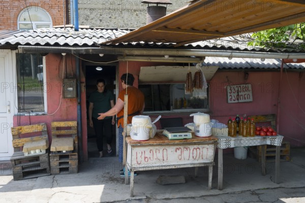A rustic market stall with handmade products and people talking, selling cheese and tomatoes and homemade specialties, Badiauri, Kakheti region, Georgia