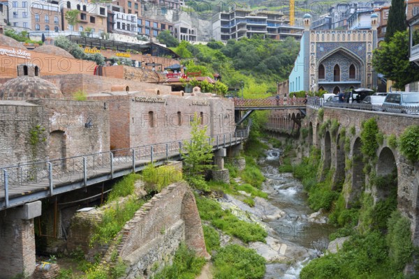Historic bridge over a river surrounded by lush vegetation, Leghvtakhevi river and gorge, Orbeliani Bath on the right, King Erekles Bath, sulfur baths, Abanotubani spa district, old town, Tbilisi, Tbilisi, Georgia