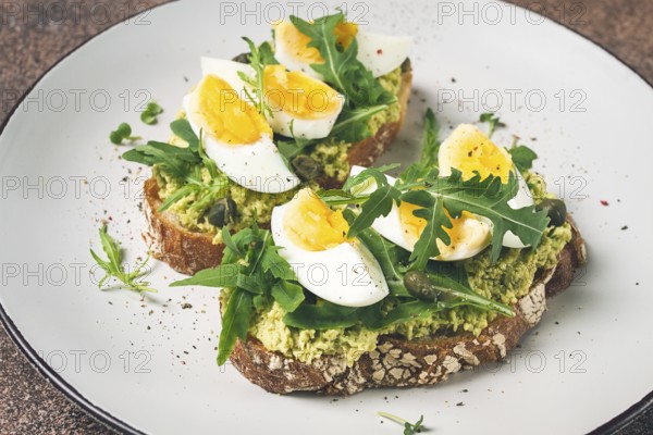 Sandwich with mashed avocado, boiled egg, and arugula, on bread, homemade, breakfast