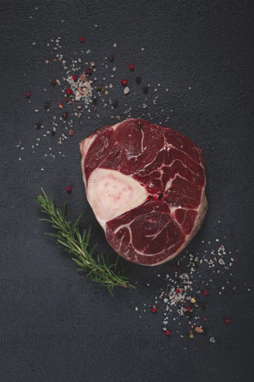 A shank on the bone, raw meat for ossobuco, on the table, with a branch of rosemary, top view, no people