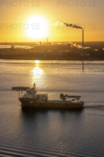 Offshore workship EDT Prometheus arrives at the mouth of the Weser, in the background the Kronos Titan chemical plant, a leading global manufacturer of titanium dioxide, in Nordenham, Bremerhaven, sunset, Germany