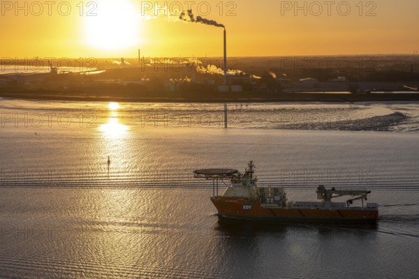 Offshore workship EDT Prometheus arrives at the mouth of the Weser, in the background the Kronos Titan chemical plant, a leading global manufacturer of titanium dioxide, in Nordenham, Bremerhaven, sunset, Germany