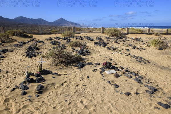 View of old sanded historic cemetery from the 1950s with several graves marked by stones from the abandoned village village of Cofete on the west coast of the Jandia peninsula, in the background Atlantic, Cofete, Jandia, Las Palmas province, Fuerteventura, Canary Islands, Spain