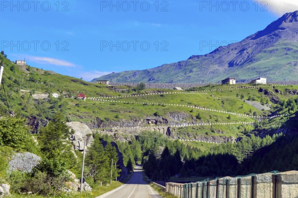 Road from in Italy just in front of the border with France, in the background driveway with switchbacks to the Alpine Pass Col de Mont Cenis pass road. Above crown of Lac de Mont Cenis dam, Moncenisio, Piedmont region, Italy, Mont Cenis, Savoy, France