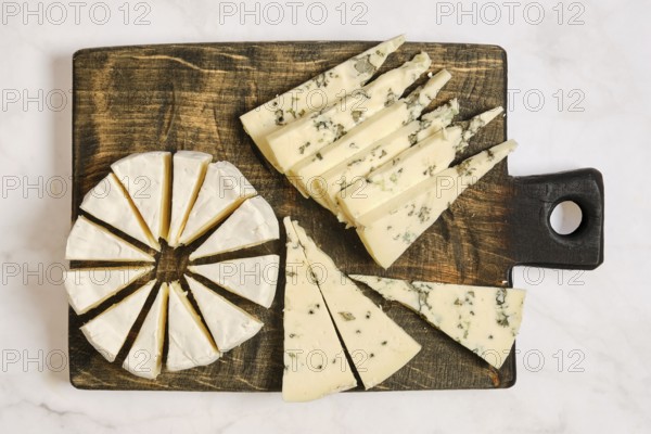 Different types of cheese are arranged on a wooden board. One cheese is round and cut into wedges. Another type is sliced into triangles. The platter displays a mix of textures and shapes