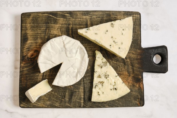 A wooden board holds pieces of cheese cut into various shapes. One piece is partially sliced, showing a soft texture. This setting suggests a light snack during a gathering at home
