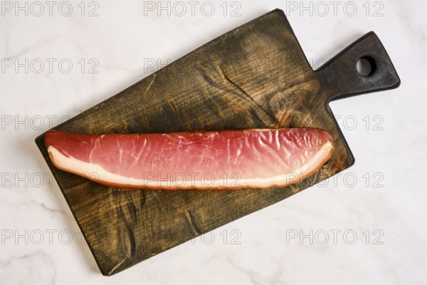 A long piece of cured parma ham on a wooden cutting board. The board has a rustic design and is placed on a light-colored surface