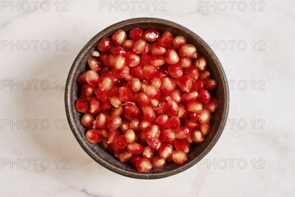 A bowl is filled with bright red pomegranate seeds. These seeds are fresh and cut from the fruit. They are ready to be used in dishes or eaten as a snack