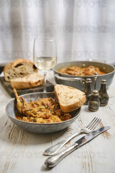 A dinner table is prepared with a bowl of food, a glass of white wine, and slices of bread. Other servings are placed nearby, creating a warm atmosphere for a meal