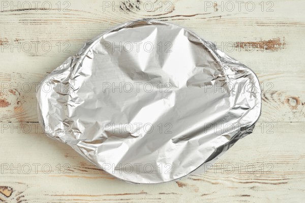 A roasting pot is covered with aluminum foil placed on a wooden kitchen table. The foil prevents excess browning while baking. It is part of a cooking activity in a home setting