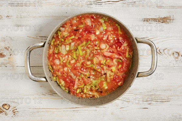A pot filled with a mixture of chopped vegetables and tomatoes on a wooden kitchen counter. The food is being prepared for a meal, showcasing various colors and textures