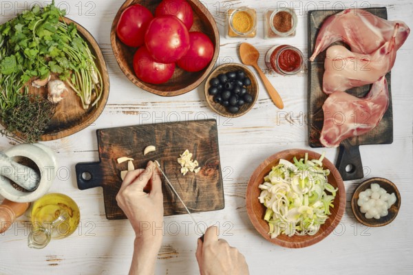 A person is chopping garlic while other ingredients are ready for cooking. Various spices sit nearby for seasoning