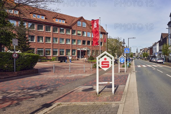 Sparkasse Schwelm-Sprockhövel, savings bank branch, advertising flags on flagpoles, advertising stele, general architecture, residential and commercial buildings, brick buildings, parking strips with vehicles, lantern, trees, hedge, pedestrian crossing, zebra stripes, slightly diffused light, slightly sunny, milky blue sky, cumulus clouds, cirrostratus clouds, street main street, Sprockhövel, Ennepe-Ruhr-Kreis, North Rhine-Westphalia, Germany