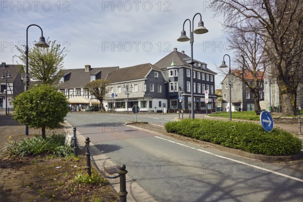 Residential and commercial buildings, houses, general architecture, half-timbered house, street, barrier chain, central island, flower beds, trees, milky blue sky, diffused light, slightly sunny, intersection of main street with Mühlenstraße, Sprockhövel, Ennepe-Ruhr district, North Rhine-Westphalia, Germany