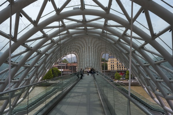 View through the modern glass bridge across a river with urban surroundings, Peace Bridge, Tbilisi, Tbilisi, Kura River, Georgia