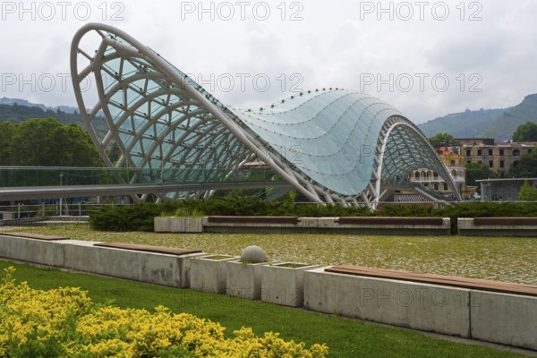 Modern glass roof of a bridge in wave form with surrounding park area, Peace Bridge, Rike Park, Tbilisi, Kura River, Georgia