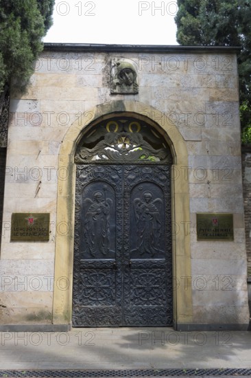 Decorated iron gate in a stone wall with plaques and surrounded by trees, entrance to the Georgian Patriarchate, the headquarters of the Georgian Orthodox Church, Tbilisi, Georgia